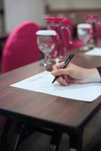 una mano sosteniendo un bolígrafo en un pedazo de papel sobre una mesa en favehotel Malang, en Malang