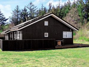 a small black house with a wooden deck in a field at 8 person holiday home in Brovst in Brovst