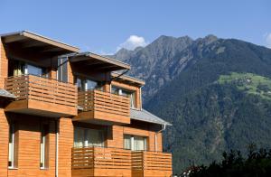 a wooden building with balconies and mountains in the background at mittendorf klimaresidence in Schenna
