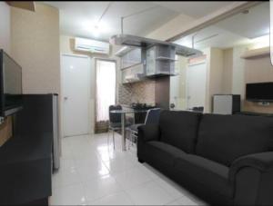 a living room with a black couch and a kitchen at Kalibata city by Sang Living in Jakarta