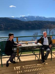 Due uomini seduti su una panchina di fronte a un lago di Ferienwohnungen Klinar a Millstatt