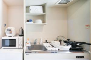 eine kleine Küche mit einer Spüle und einer Mikrowelle in der Unterkunft Comfort CUBE PHOENIX S KITATENJIN in Fukuoka