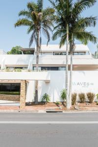 a white building with palm trees in front of it at Waves Byron Bay in Byron Bay