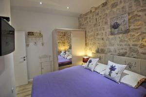 a bedroom with a purple bed with a stone wall at L & L Old Town Apartments in Dubrovnik