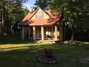 a yellow house with a red roof in a yard at Ranna Talu Puhkemaja in Kassari