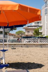 una sombrilla naranja y sillas en la playa en Appartamenti Lignano Sabbiadoro - Villa Ammiraglia en Lignano Sabbiadoro