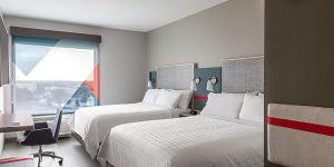 ナッシュビルにあるavid hotels - Nashville Airport, an IHG Hotelのベッド2台、デスク、窓が備わるホテルルームです。