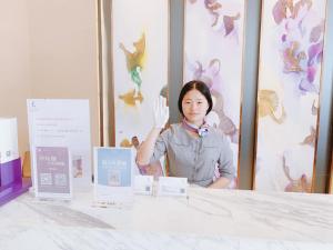 Une femme debout derrière une table avec sa main dans l'air dans l'établissement Lavande Hotel Huizhou Xinxu Government Square, à Niu'ao