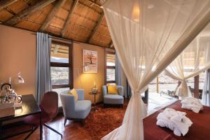 a bedroom with a bed with curtains and chairs at Hoodia Desert Lodge in Sesriem