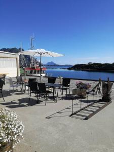 a patio with tables and chairs and a boat on the water at Kaikanten Kro og Rorbu in Sennesvik