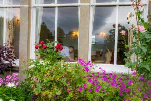 Ein Mann, der mit Blumen aus dem Fenster schaut. in der Unterkunft Coul House Hotel in Contin