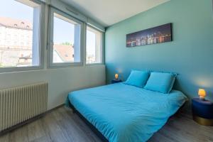a bedroom with a bed with blue sheets and two windows at Le 15-GregIMMO-Appart'Hôtel in Montbéliard