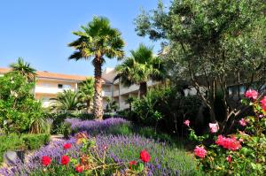 a garden with flowers and palm trees in front of a building at Residence Residhotel Mayflower in Le Grau-du-Roi