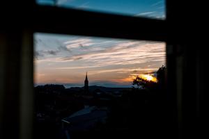 a view of a sunset from a window with a clock tower at Pousada San Clemente Centro in Gramado
