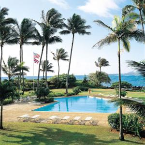 a swimming pool with palm trees and the ocean at Lae Nani Kauai in Kapaa