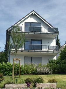 ein weißes Haus mit einem Balkon und einer Bank in der Unterkunft Ferienwohnungen Pellenzblick - Wohnen auf Zeit - in Nickenich