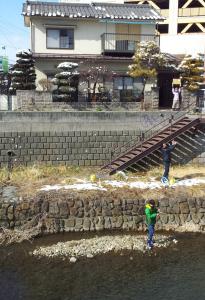 zwei Personen stehen an einer Steinmauer neben einem Haus in der Unterkunft Matsumoto BackPackers in Matsumoto