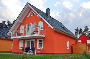 uma casa vermelha com uma varanda e um cão na varanda em Ferienhaus Müritzbrise / EG-Appartement em Marienfelde