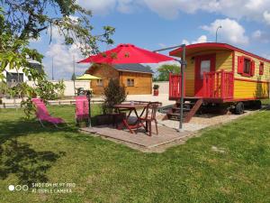 a tiny house with a table and a red umbrella at roulotte du domaine des Chevrettes in Cour-Cheverny