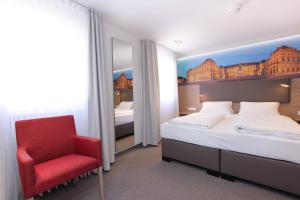 a bedroom with a bed and a red chair at City Hotel Würzburg in Würzburg