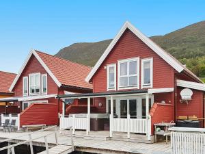 a red house with a wooden deck and mountains in the background at 6 person holiday home in Gursken-By Traum in Larsnes