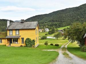ein gelbes Haus auf einem grünen Feld mit einer unbefestigten Straße in der Unterkunft Holiday Home Nedre II in Eidsdal