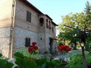 an old stone building with red flowers in the foreground at Agriturismo Santa Giuditta in Sovicille