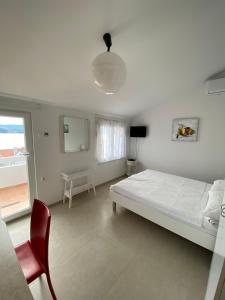 ein weißes Schlafzimmer mit einem Bett und einem roten Stuhl in der Unterkunft Apartmani Marko in Baška