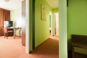 Zimmer mit grünen Wänden, einem Tisch und einem Schreibtisch in der Unterkunft Hotel Mondial in Langenfeld