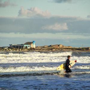 a man walking into the ocean with a surfboard at Cabañas Kundalini Punta del Diablo in Punta Del Diablo