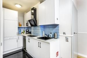 una cocina con armarios blancos y azulejos azules en JessApart– Babka Tower Apartment, en Varsovia