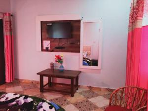 a living room with a table and a tv on the wall at Pahadi Ghar Homestay in Kanatal