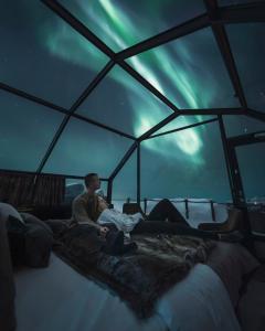 a couple of people sitting on a bed under the northern lights at Golden Crown - Levin Iglut in Levi