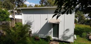 a white shed with a door in a yard at Alexandra Headland in Alexandra Headland