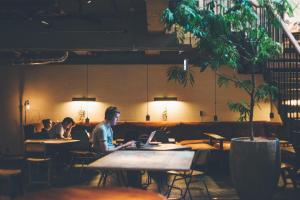 two people sitting at tables in a restaurant with their laptops at CITAN Hostel in Tokyo