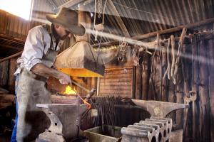 Een man met een hoed maakt een metalen voorwerp. bij Holowiliena Station & The Outback Blacksmith in Flinders Ranges