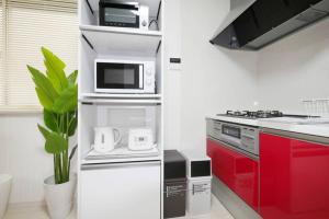 Biała kuchnia z czerwonymi szafkami i kuchenką mikrofalową w obiekcie アンドステイ高砂2丁目 w Tokio