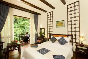 - une chambre avec un lit et une femme assise dans une chaise dans l'établissement Mai Chau Lodge, à Mai Châu