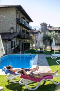 two people laying on chaises next to a swimming pool at Hotel Antica Croce - Gardaslowemotion in Tenno