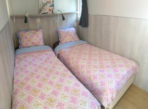 twee bedden in een kleine kamer met roze dekens bij Chalet Hoenderloo Beuk in Hoenderloo