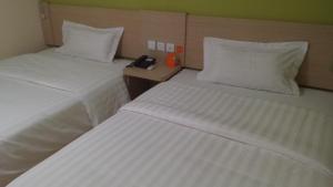 two beds in a hotel room with a phone on a table at 7Days Inn Nanan Shuitou southeast Fortune Plaza in Quanzhou