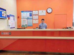 a man standing behind a counter with a clock at 7Days Inn Shijiazhuang Friendship Avenue Jianguo Road in Shijiazhuang