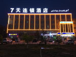 een gebouw met een verlicht bord op een parkeerplaats bij 7Days Inn Aksu Airport in Wensu