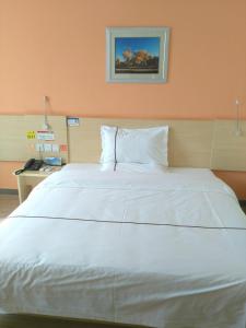 uma grande cama branca num quarto com uma parede laranja em 7Days Inn Aksu Airport em Wensu