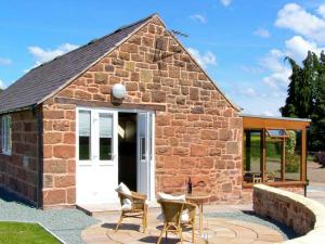 a brick building with a white door and a patio at Byre Cottage in Nesscliffe