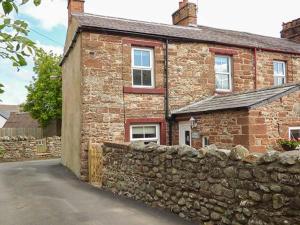 a brick house with a stone wall next to a street at Bakers Cottage in Newbiggin