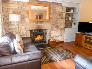 a living room with a leather couch and a stone fireplace at Deskford Cottage in Balblair