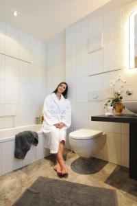 una mujer en un albornoz sentada en un inodoro en un baño en Hotel Christl, en Rohrdorf