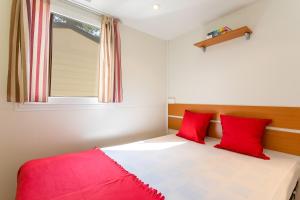 a bedroom with a bed with red pillows and a window at Camping Village Mare Pineta in Sistiana