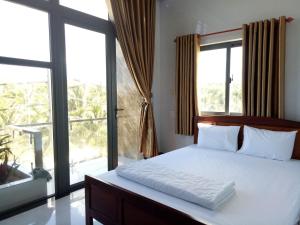 um quarto com uma cama branca e janelas grandes em Hướng Dương Hotel Đảo Phú Quý em Phú Quý